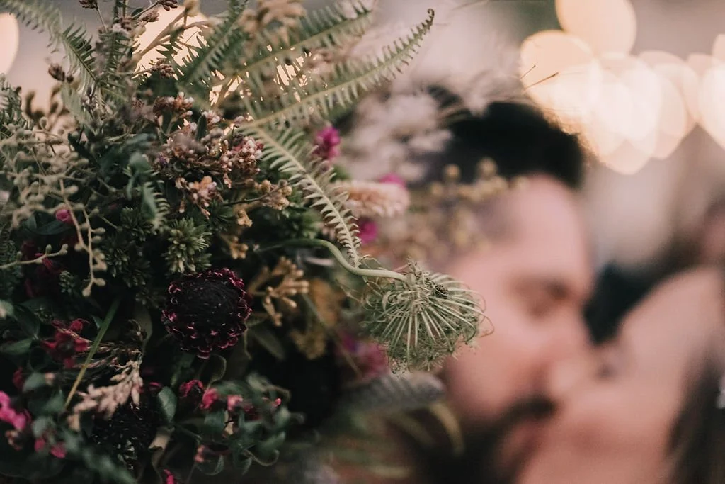 Detalhe de uma decoração com muitas plantas e flores, com uma pessoa ao fundo em foco difuso.