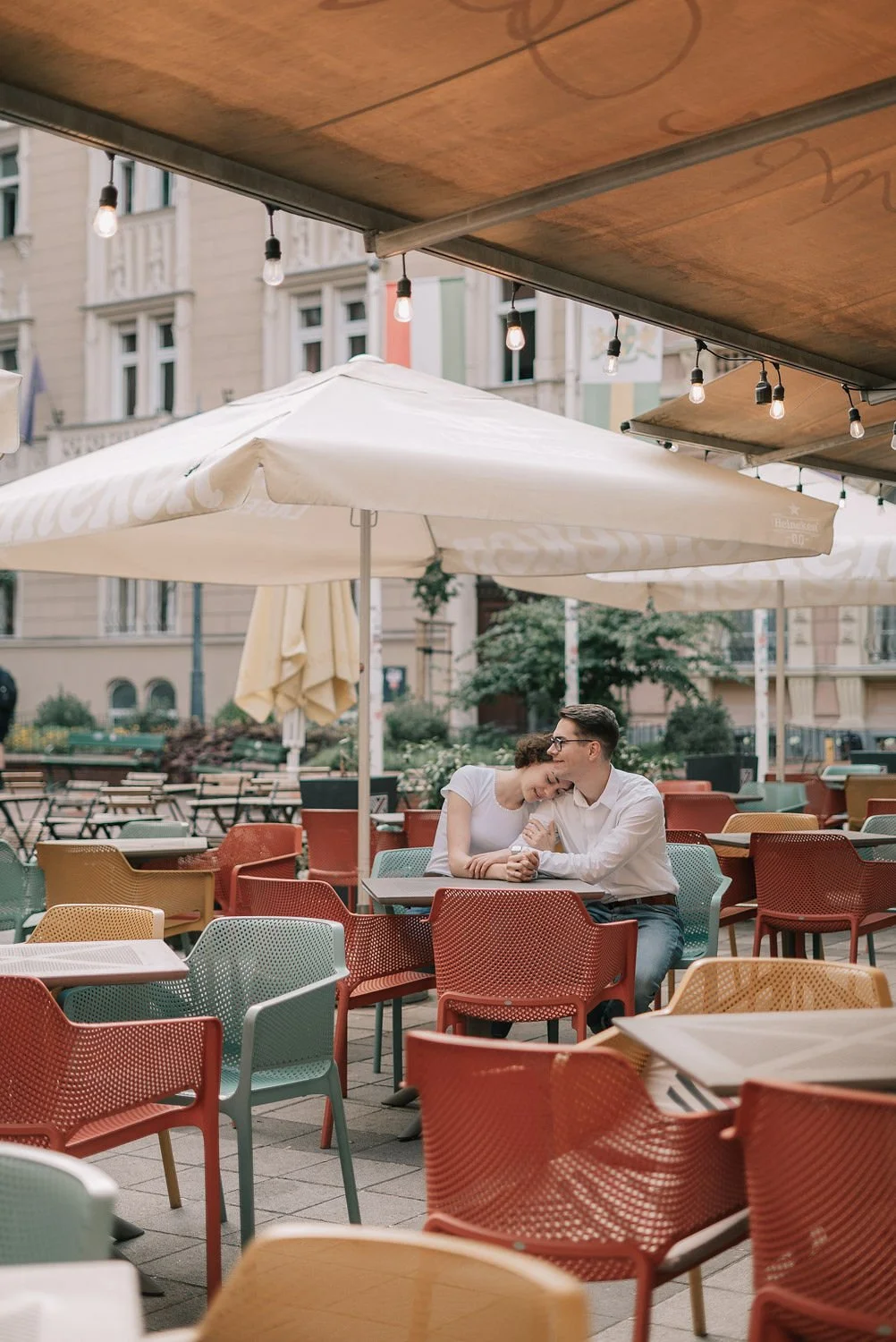 Casal sentado em um restaurante ao ar livre sob guarda-sóis e luzes de decoração.