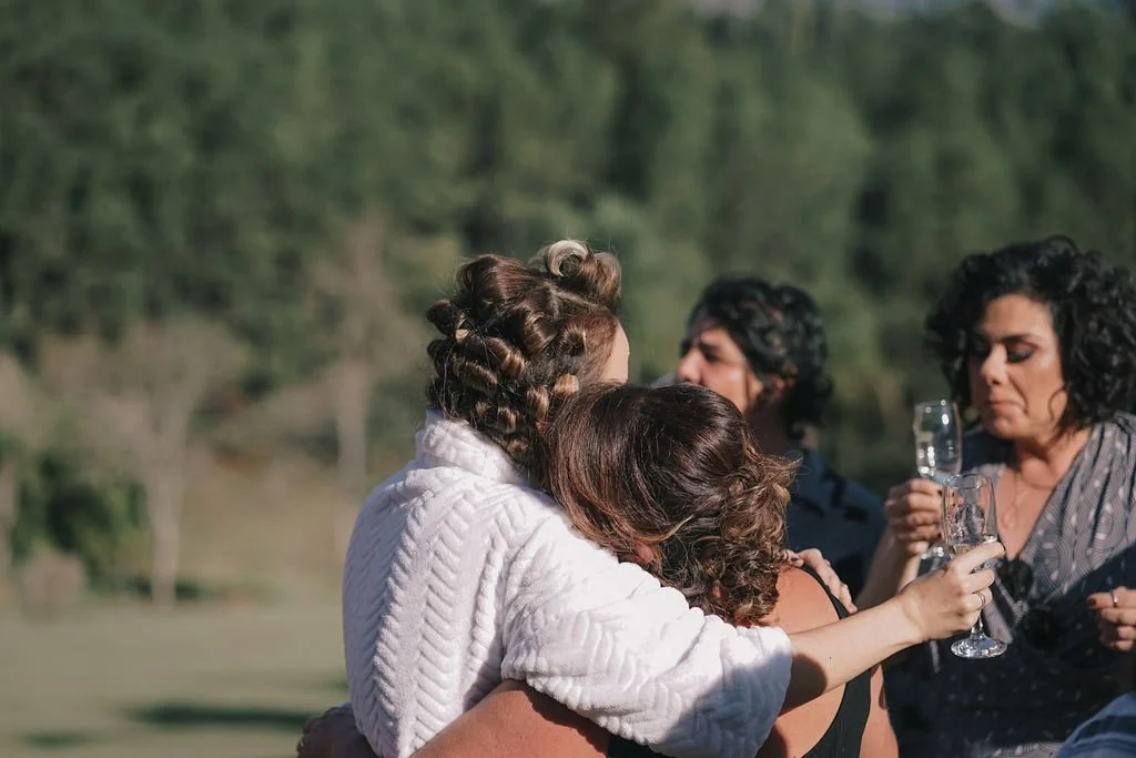 Grupo de pessoas se abraçando ao ar livre, com duas delas segurando taças de espumante.