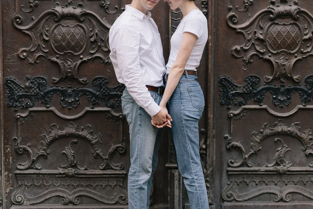Casal segurando as mãos na frente de uma porta de ferro decorada.