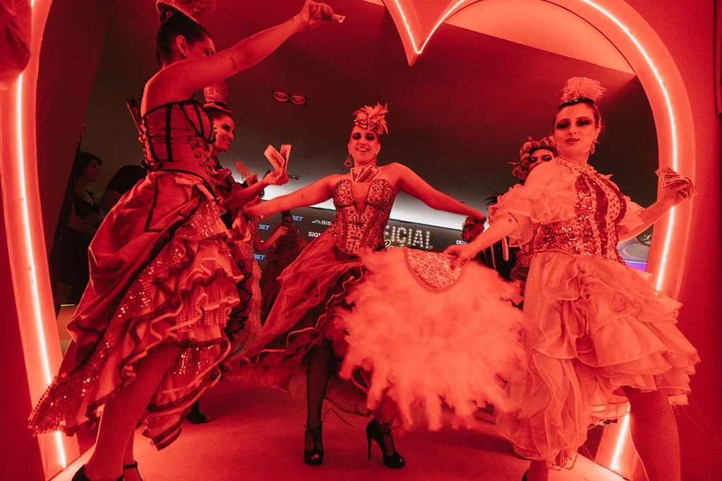 Grupo de apresentadoras de roupas tradicionais de carnaval em cenário iluminado com luz rosa e coração.