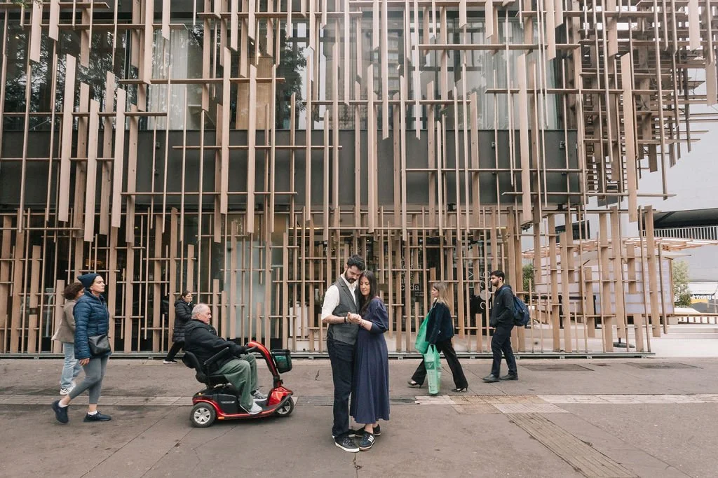 Pessoas caminhando na rua em frente a um edifício moderno com estrutura de madeira exposta.