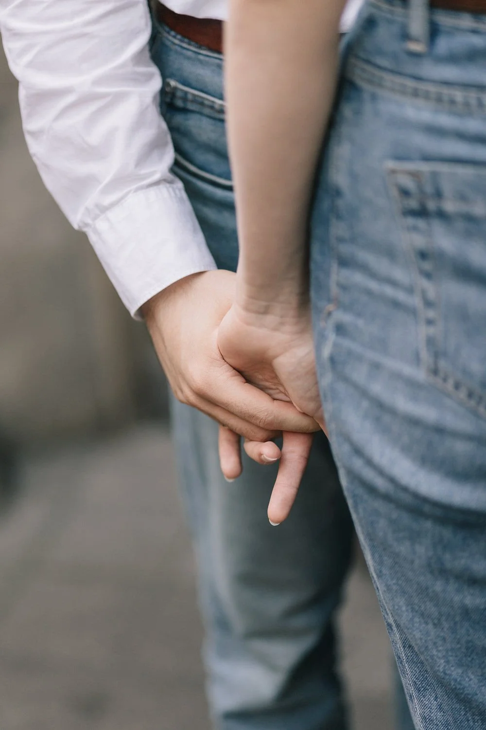 Pessoa de cabelo longo de cabelos claros e pele clara segurando a mão de alguém usando jeans e camiseta branca