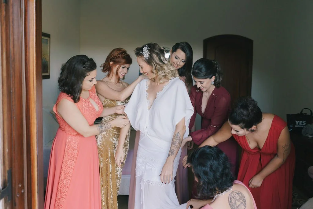 Mulheres ajudando a noiva com o vestido de casamento em um ambiente interno.