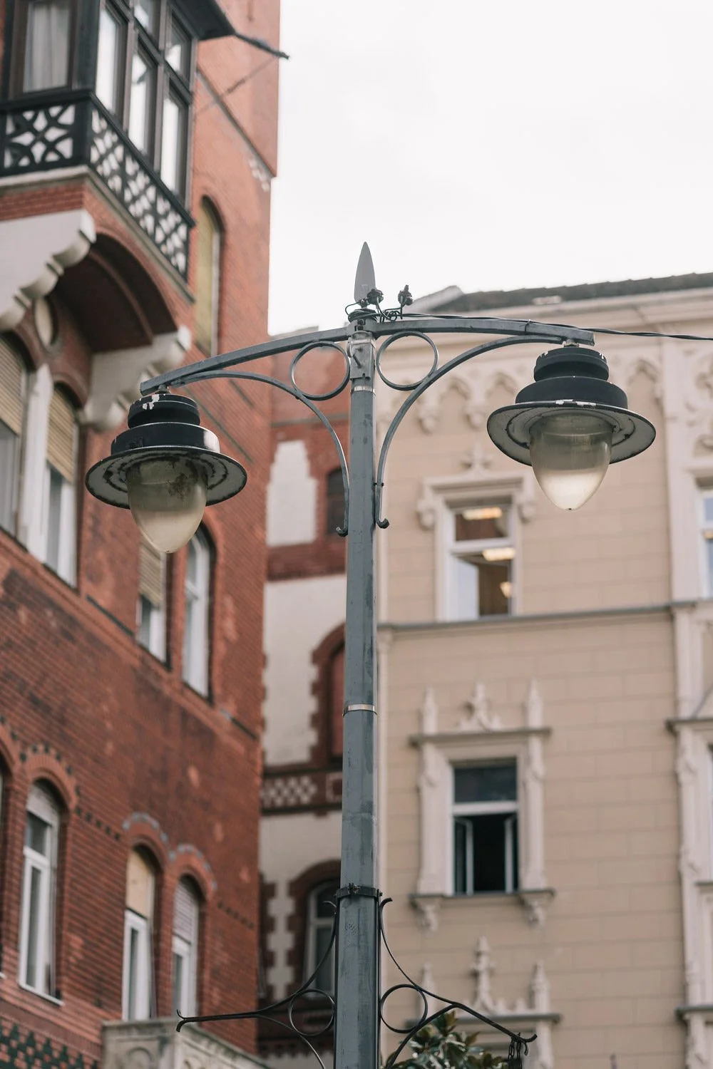 Poste de luz antigo com duas luminárias, em frente a edifícios históricos de arquitetura clássica.