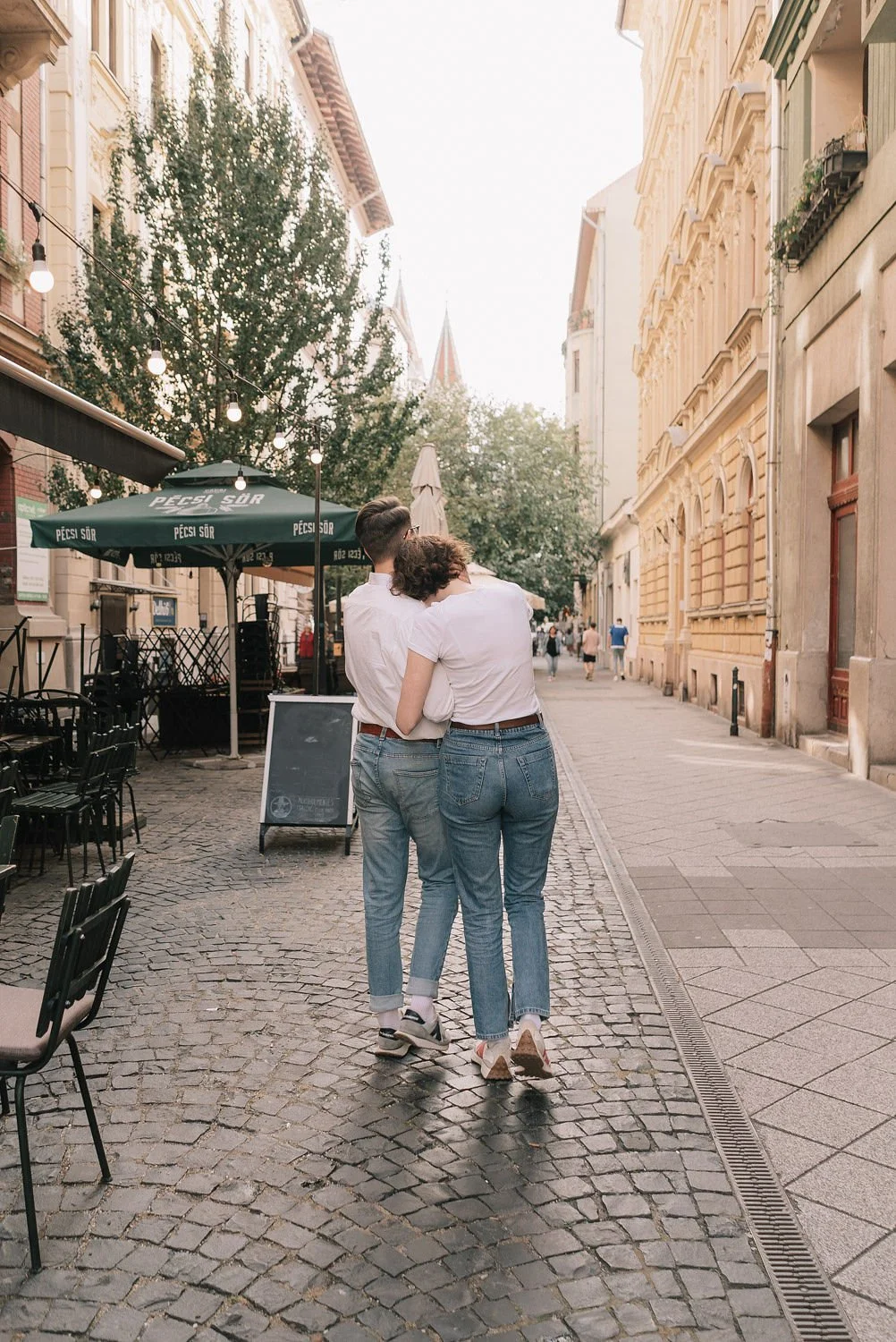 Casal caminhando de braços dados por uma rua de paralelepípedos, cercada por prédios históricos e com iluminação suave