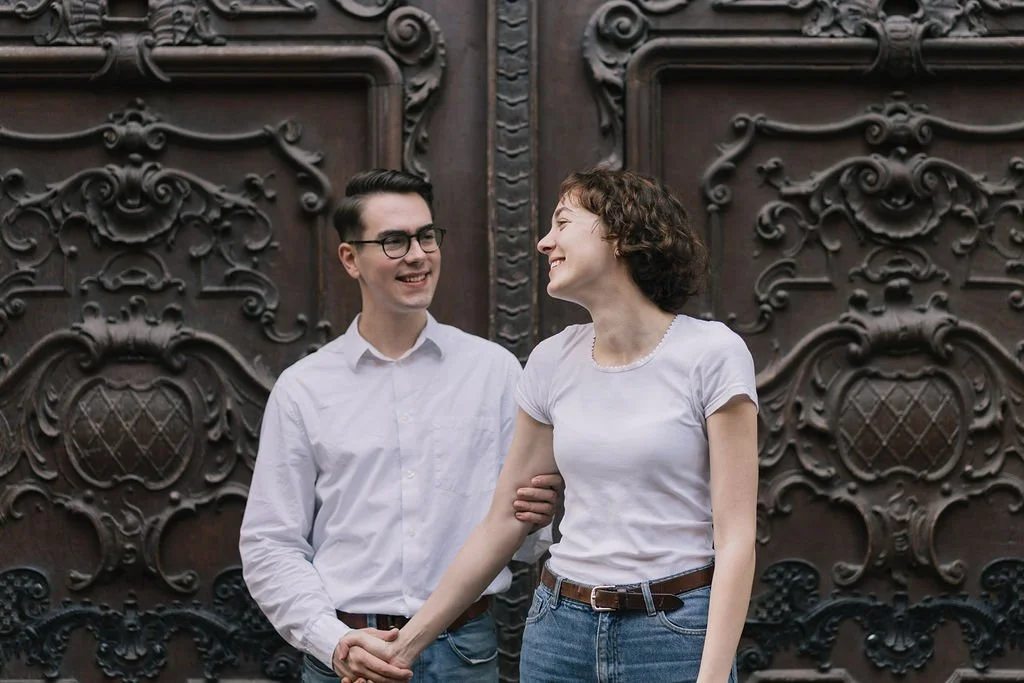 Homens e mulher sorrindo e se segurando pelas mãos em frente a uma porta de madeira decorada elaboradamente.