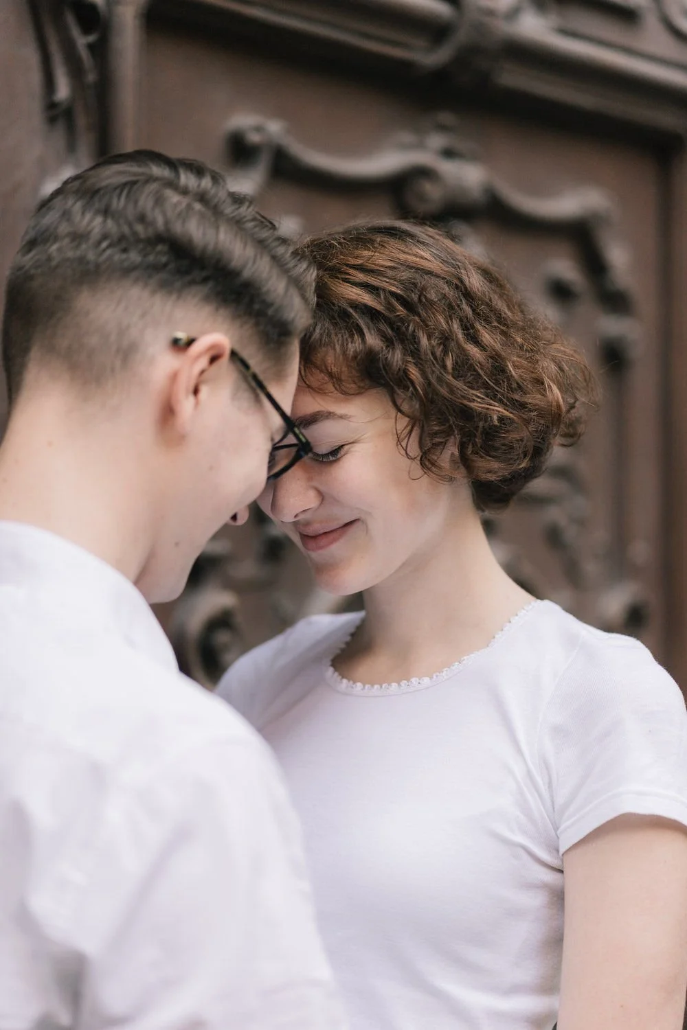 Um casal com testa encostada, sorrindo, com fundos de madeira.