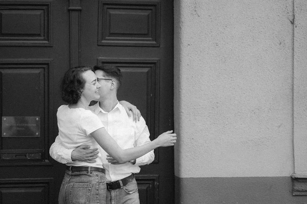 Casal se abraçando e beijando na rua, ao lado de uma parede.