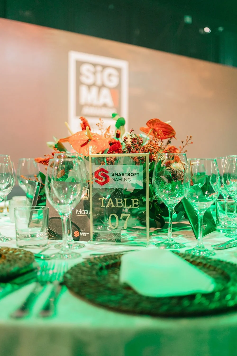 Mesa de jantar decorada com taças de vidro, um arranjo de flores vibrantes e um sinal que diz 'TABLE 07'.