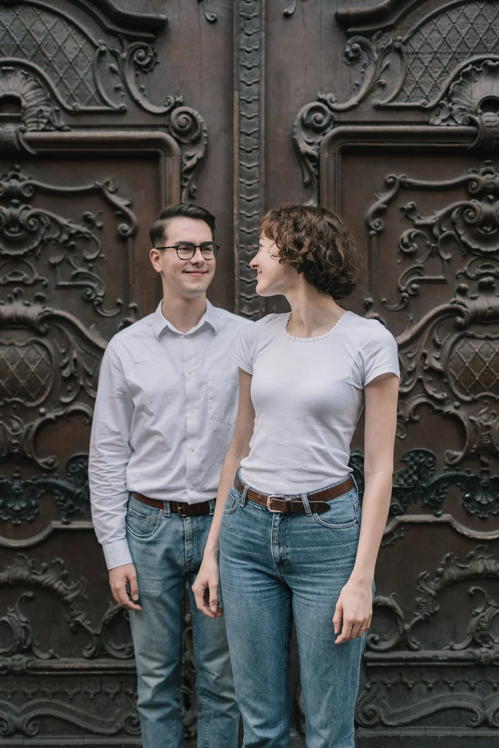Homens e mulheres sorrindo na frente de uma porta de madeira decorada com detalhes em alto relevo.