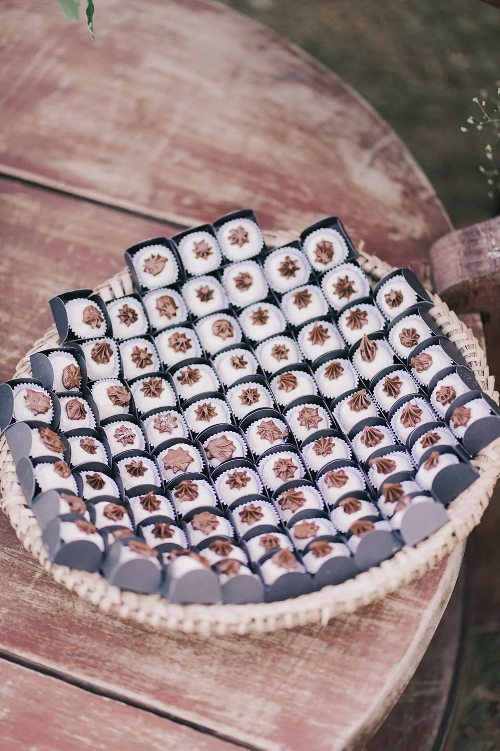 Cubos com doces de chocolate e chantilly, decorados com estrelas de chocolate, dispostos em uma bandeja redonda em uma mesa de madeira.