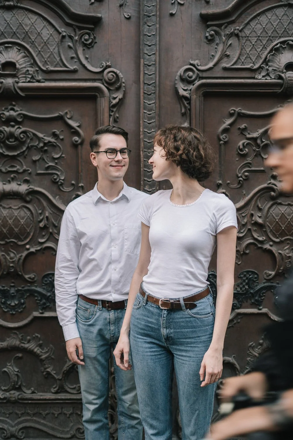 Homens e mulher sorrindo em frente a uma porta de madeira decorada com detalhes em alto relevo.