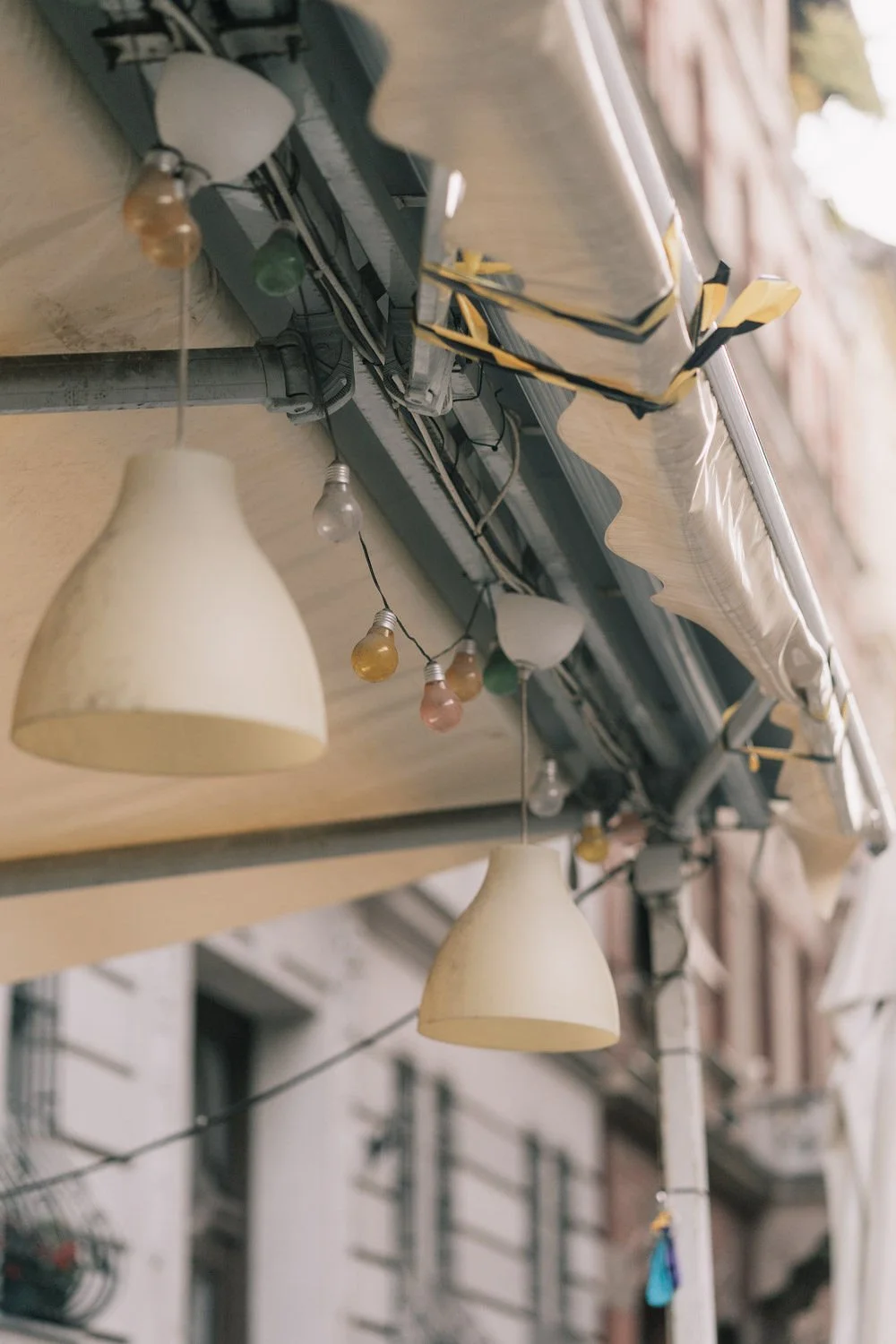 Luzes decorativas penduradas em um teto de varanda com prédios ao fundo.