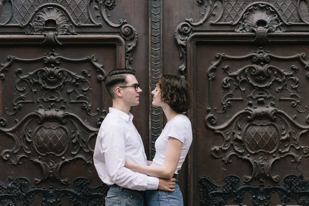 Homens e mulheres se olhando de frente em frente a uma porta de madeira com detalhes ornamentais.