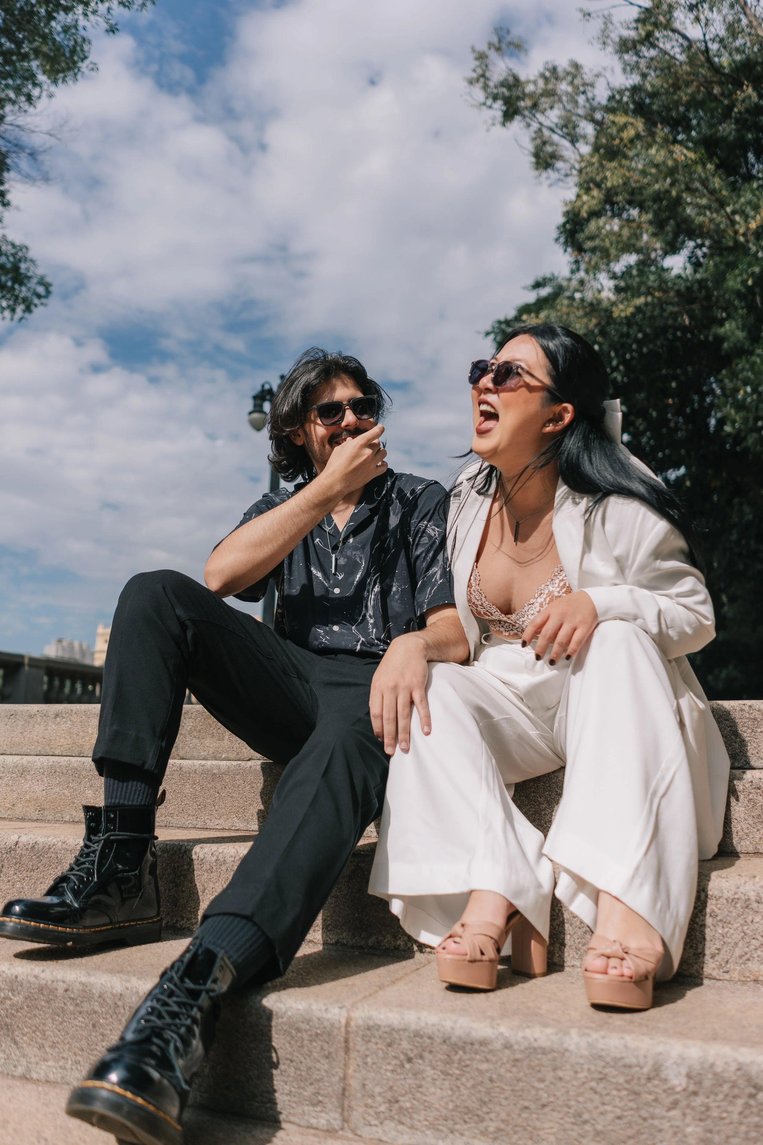 Homens e mulher sentados em escadas ao ar livre, conversando e rindo em um dia ensolarado.