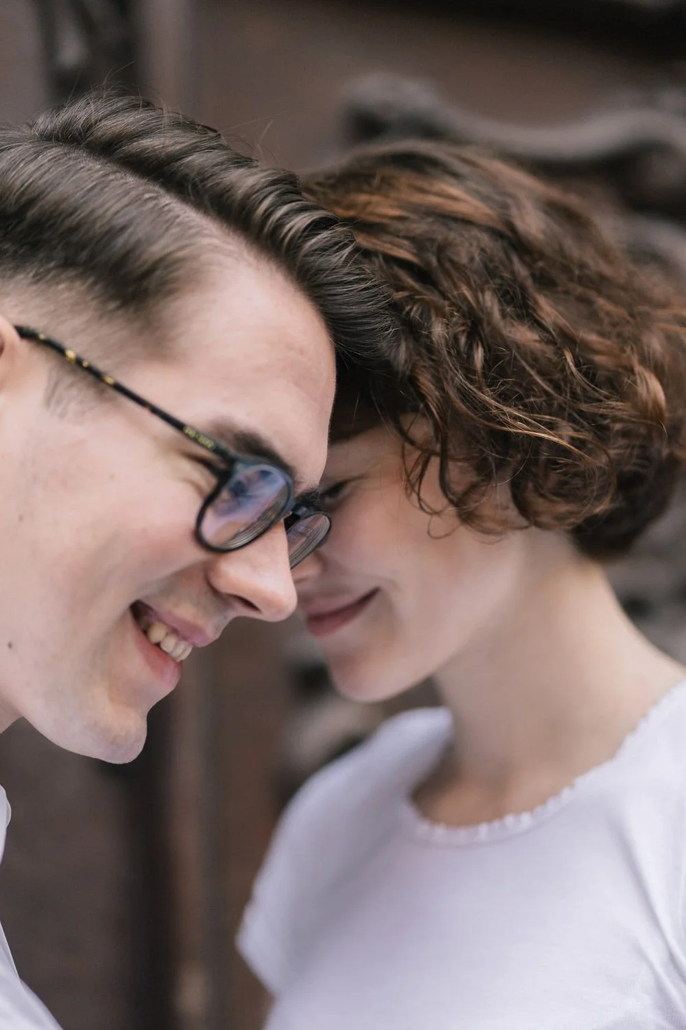 Homem e mulher com cabeças próximas, sorrindo e com o rosto de cabeça baixa, formando uma conexão íntima.
