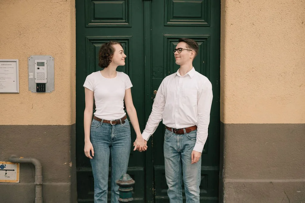 Um casal segurando as mãos na frente de uma porta verde, sorrindo um para o outro.