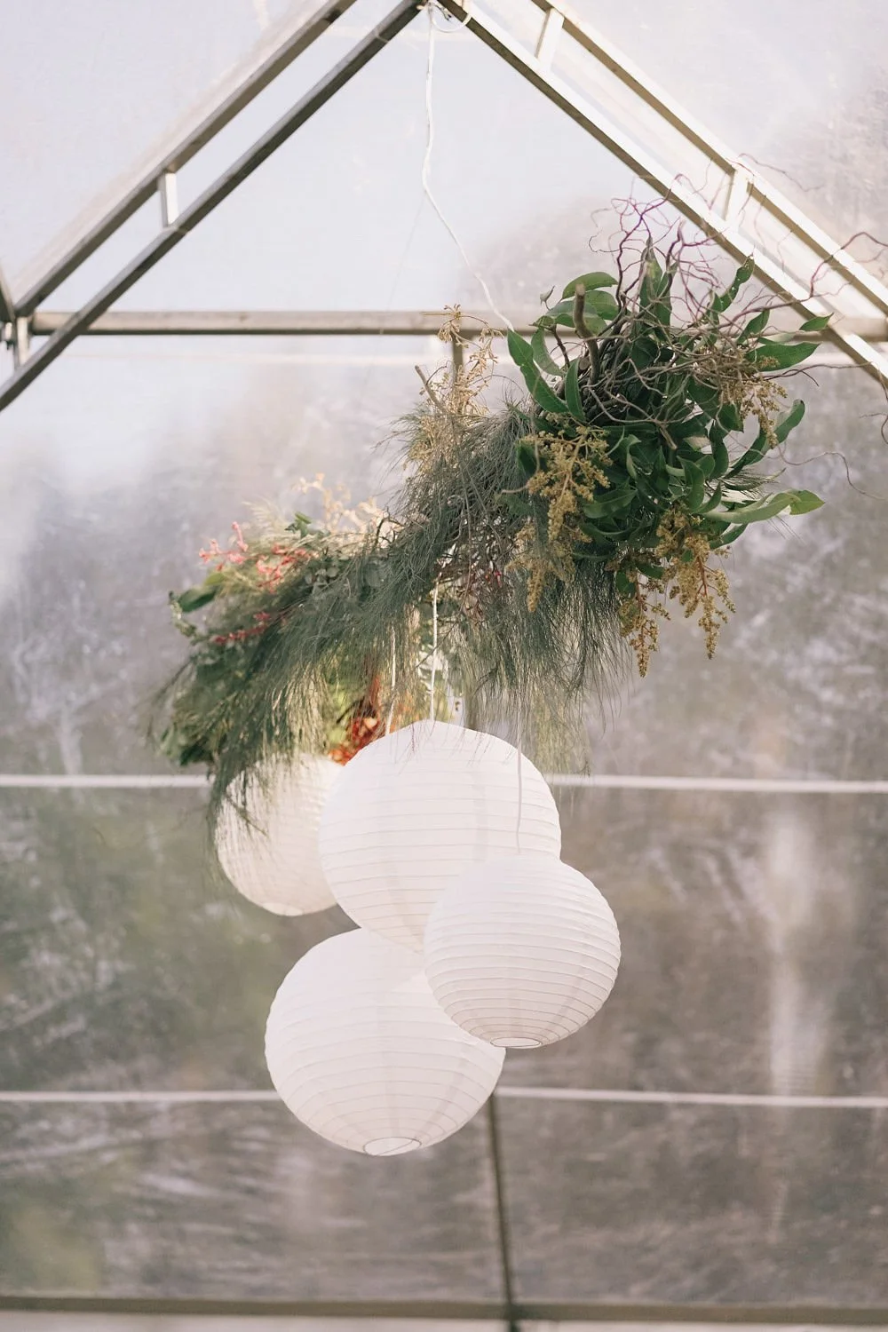 Lustre com três luminárias de papel branco e um arranjo de plantas pendurado.