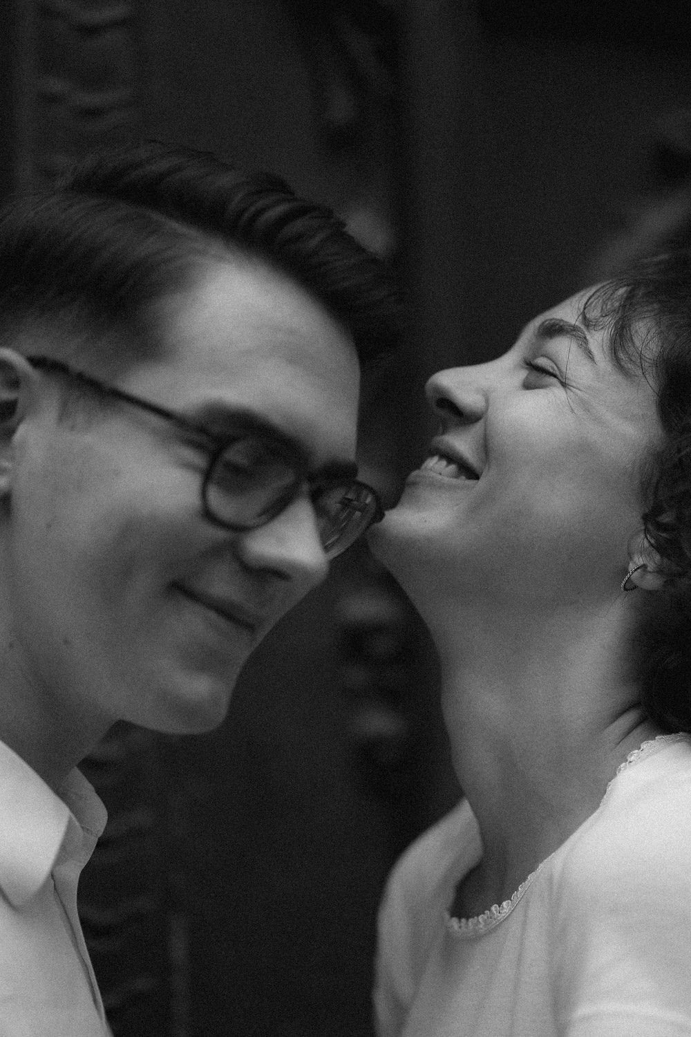 Homens sorrindo próximos, rosto quase tocando, em preto e branco.