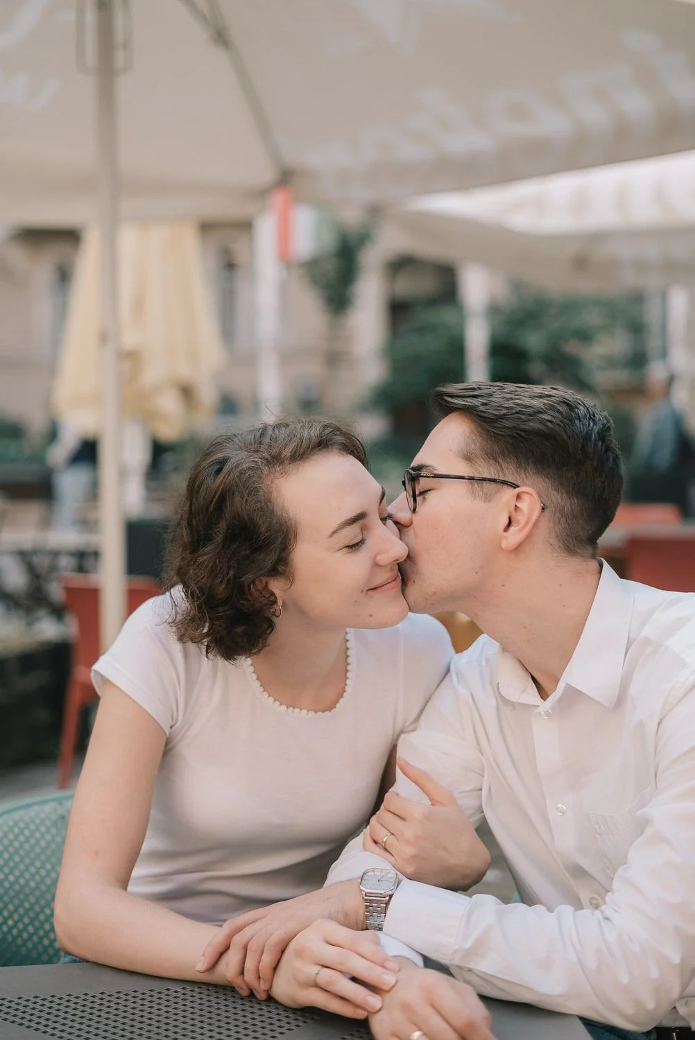 Um casal se beijando e sorrindo em um restaurante ao ar livre.