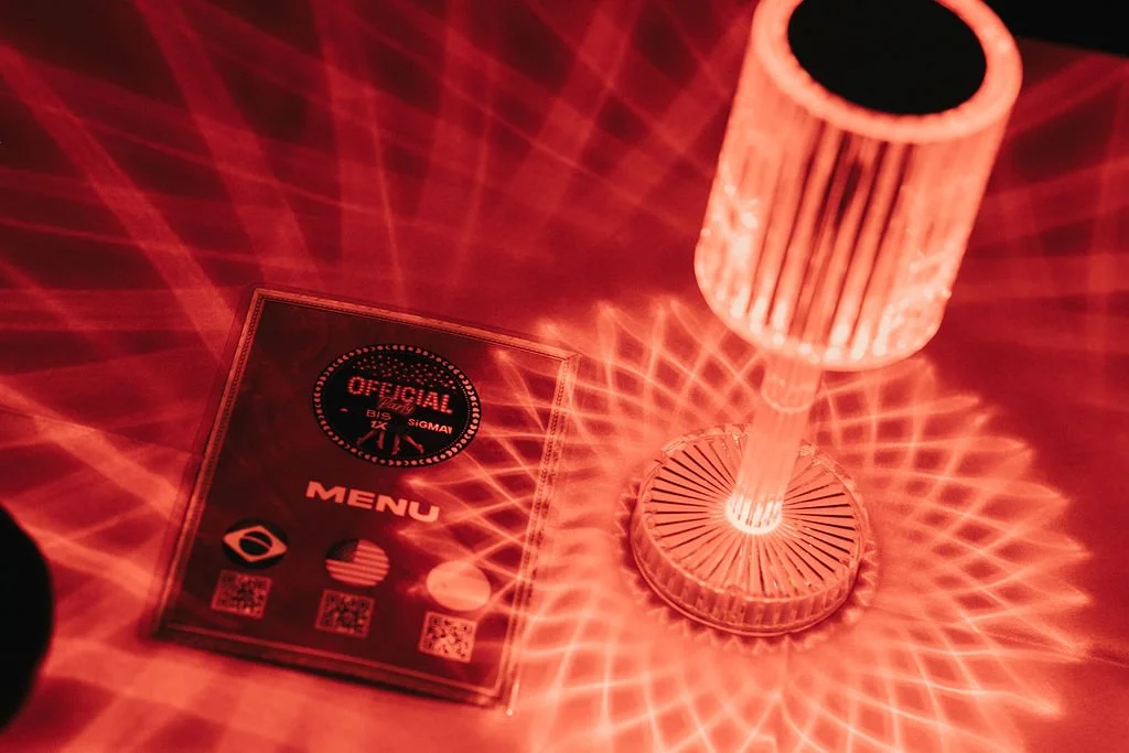 Luz de LED com efeito de padrão de laser projetada em uma mesa, próxima a um cardápio ou menu com o logotipo 'OFICIAL' e símbolos de redes sociais.