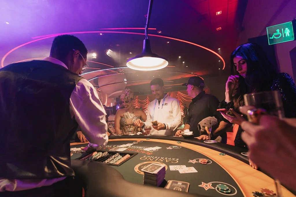 Pessoas jogando pôquer em um ambiente com iluminação colorida e uma mesa de cassino, com vários jogadores e um dealer.