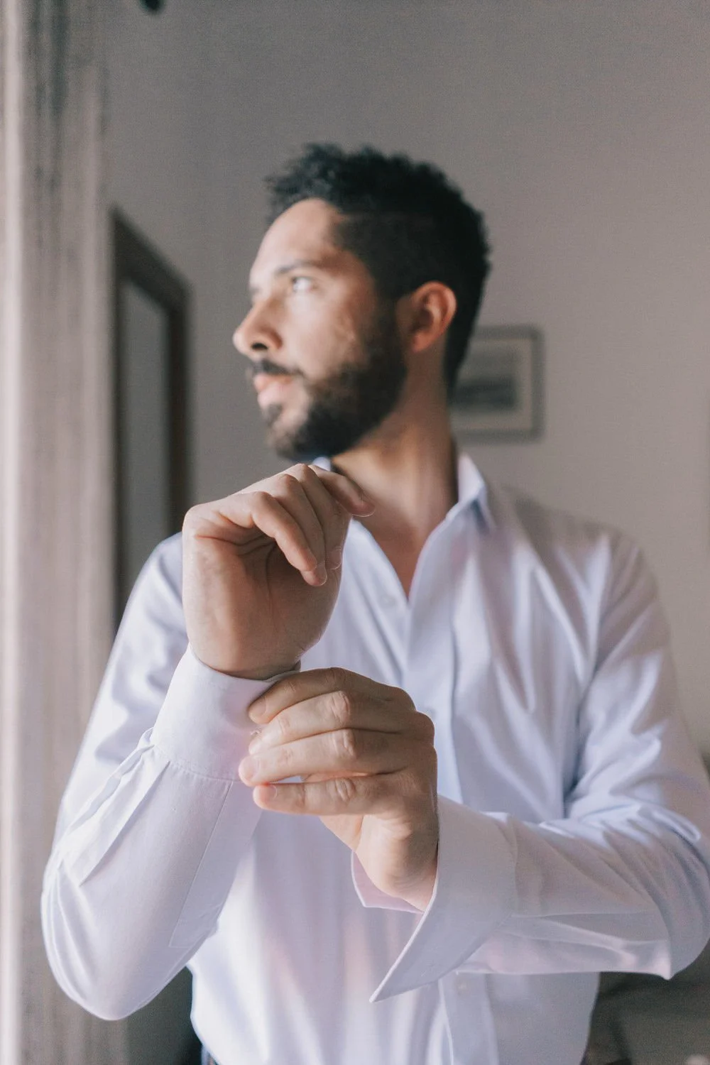 Homem penteando o punho de uma camisa branca em um ambiente interno.