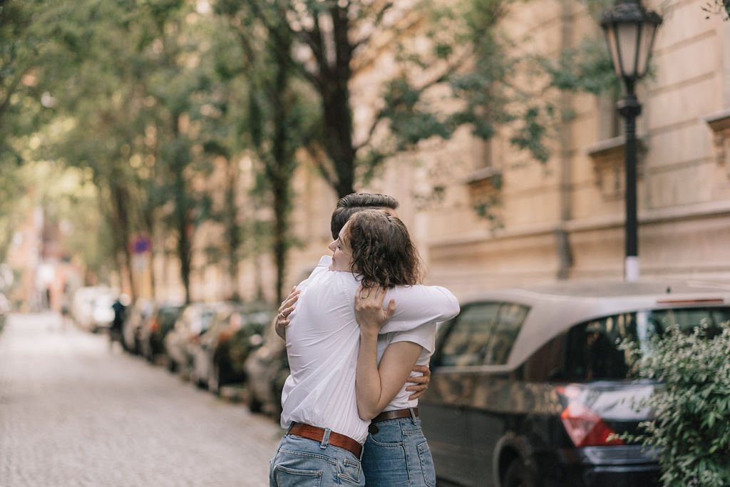 Casal se abraçando na rua, com carros estacionados ao fundo e árvores
