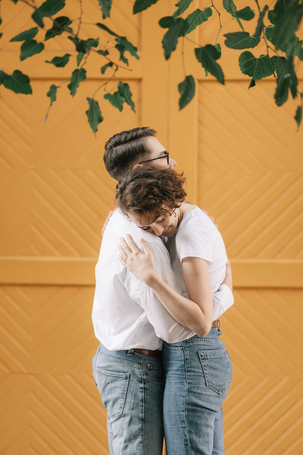 Homens e mulheres abraçando, com um fundo de parede de madeira e plantas penduradas no teto.