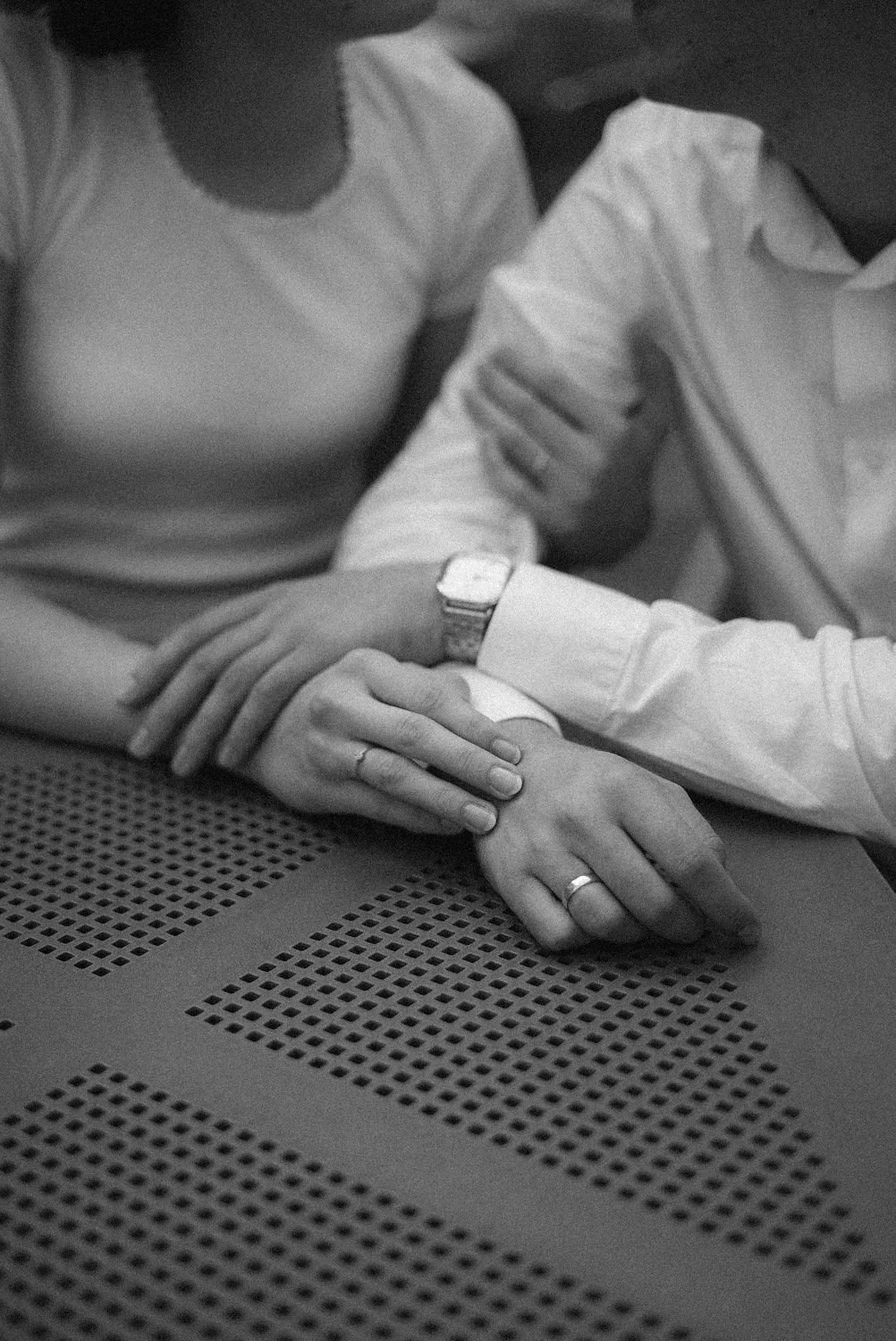 Casais se segurando pelas mãos, símbolos de união, com uma superfície perfurada ao fundo.