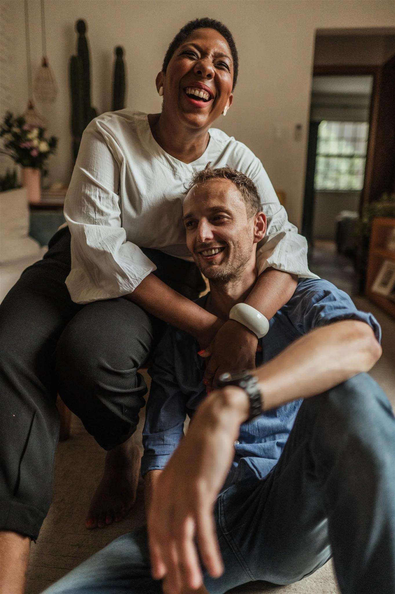 Smiling couple embracing indoors, woman sitting, man leaning on her knees.