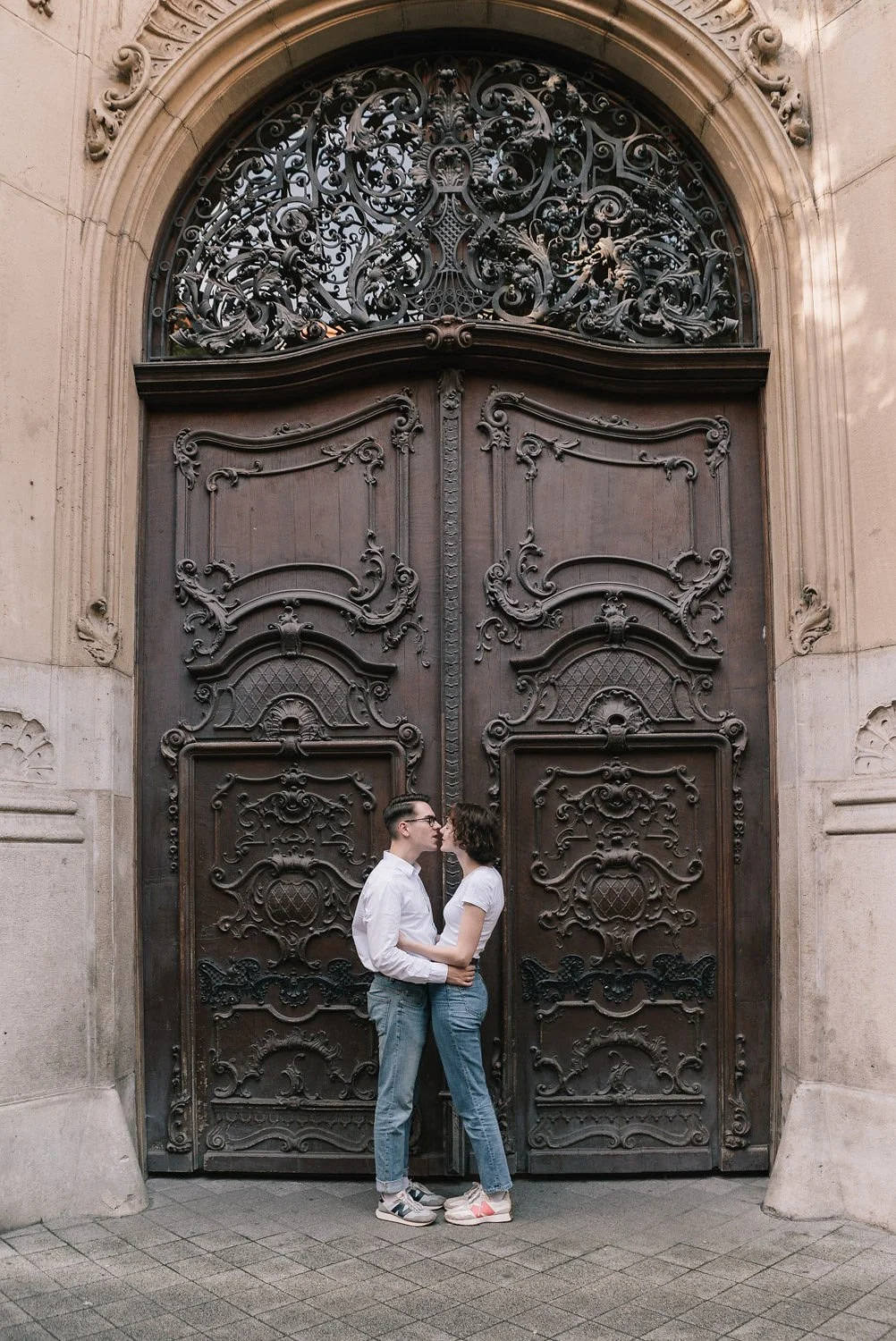 Casal se beijando em frente a uma grande porta de madeira com detalhes elaborados em ferro.