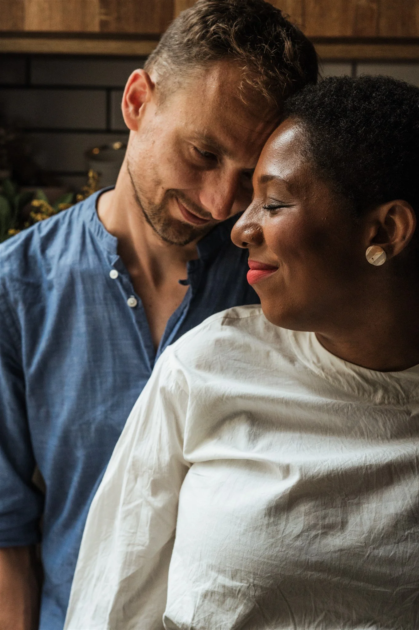 Close-up of a couple embracing, man in blue shirt leaning gently against woman in white top.