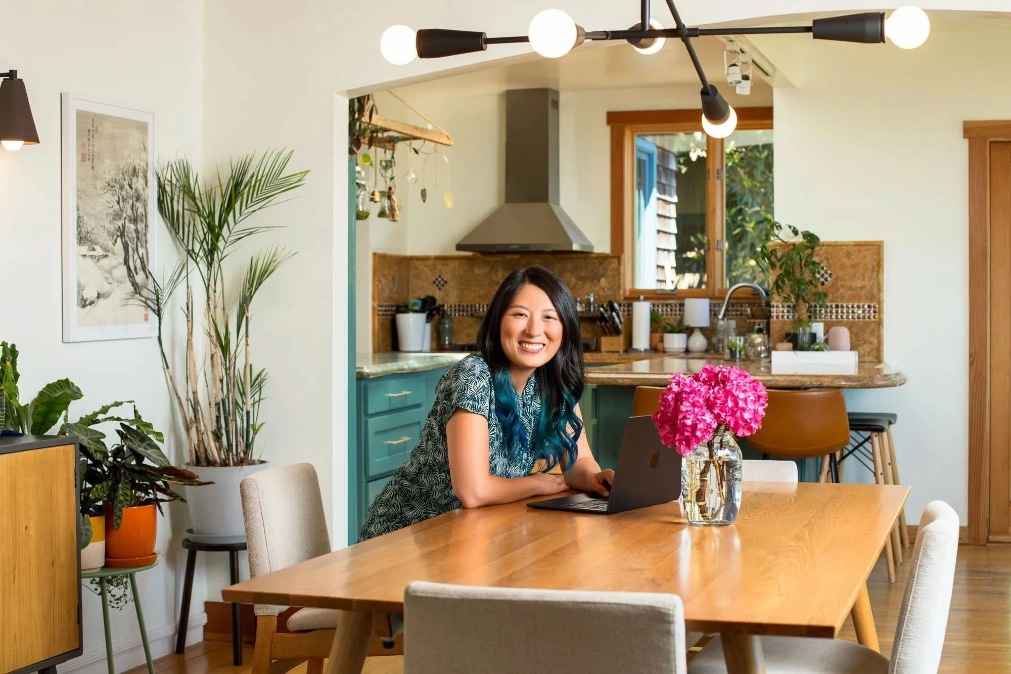 Commercial lifestyle photo of smiling woman in green shirt working on laptop at kitchen table, San Francisco Bay Area lifestyle photographer