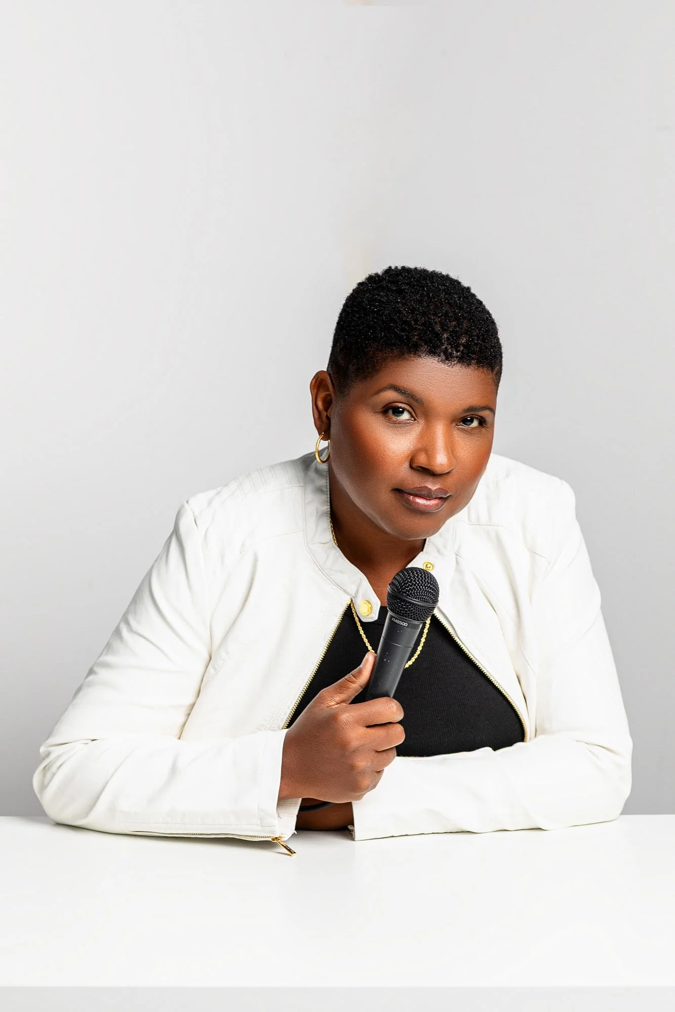 Studio portrait of Black woman in white suit with microphone, San Francisco Bay Area commercial portrait photographer for media speaker and podcast brands