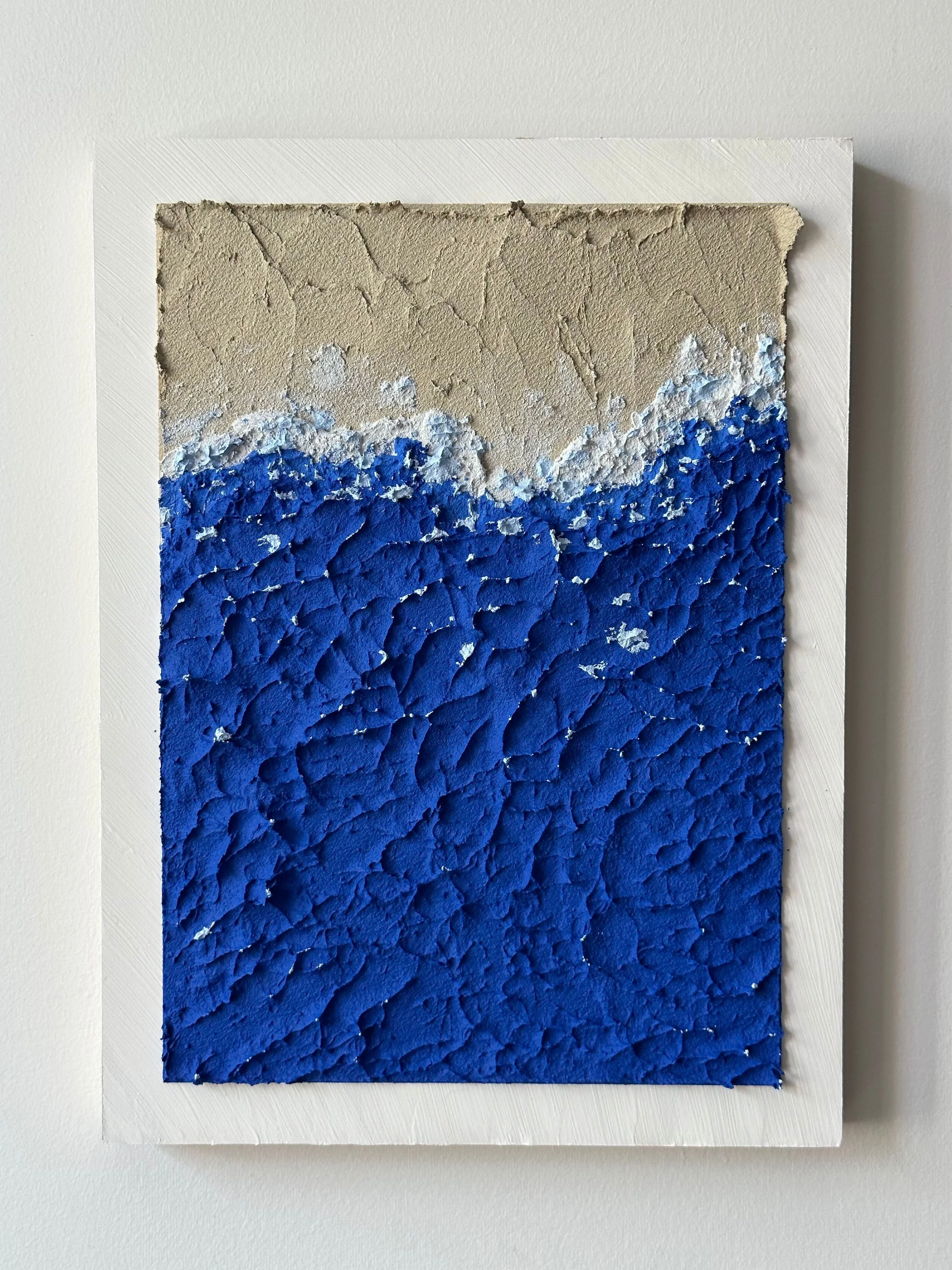 Mixed media artwork of a textured painting featuring a beige sky and dark blue ocean waves on a white framed canvas.
