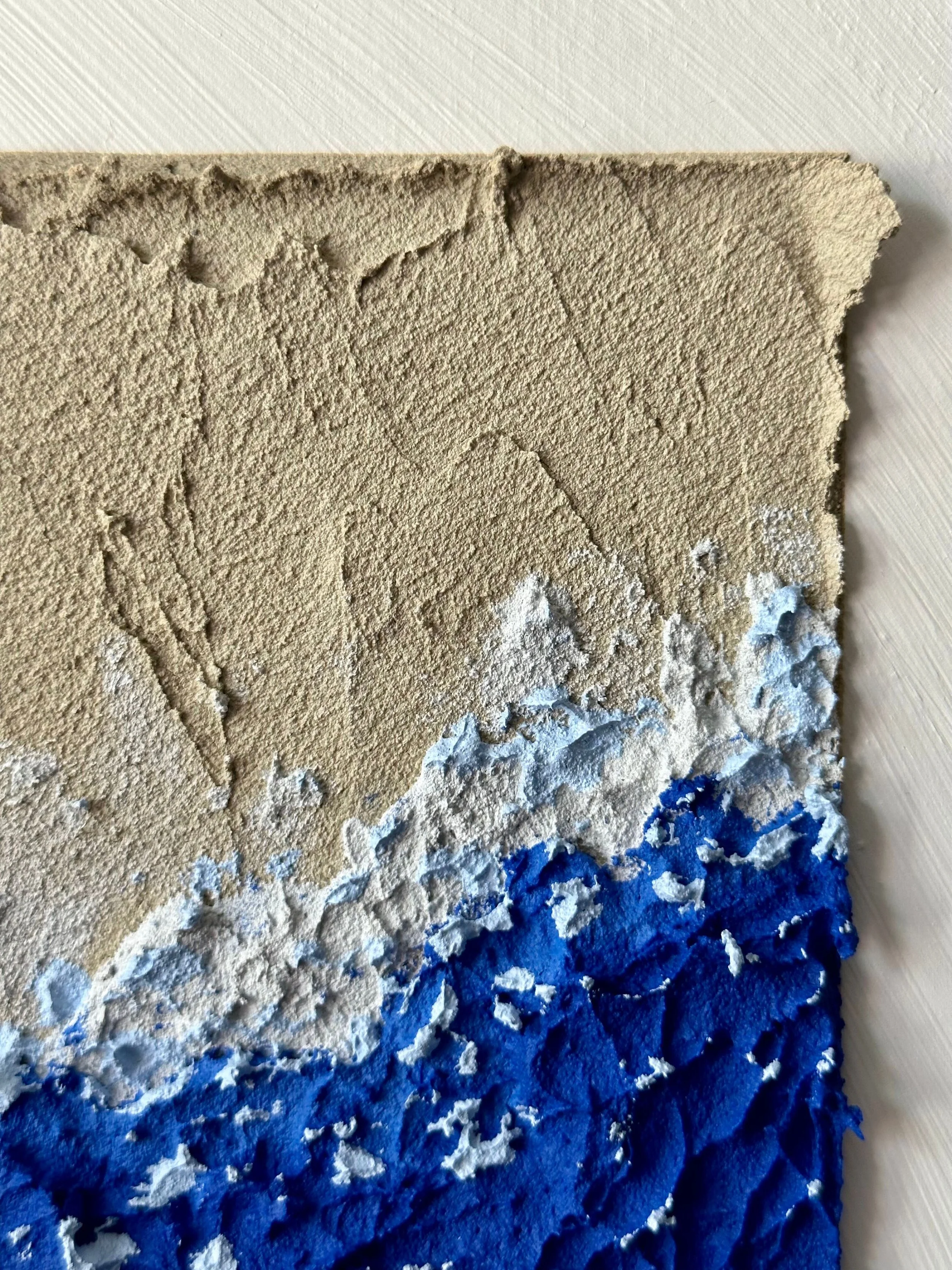 Close-up of a textured canvas with brush strokes of beige, white, and blue paint.