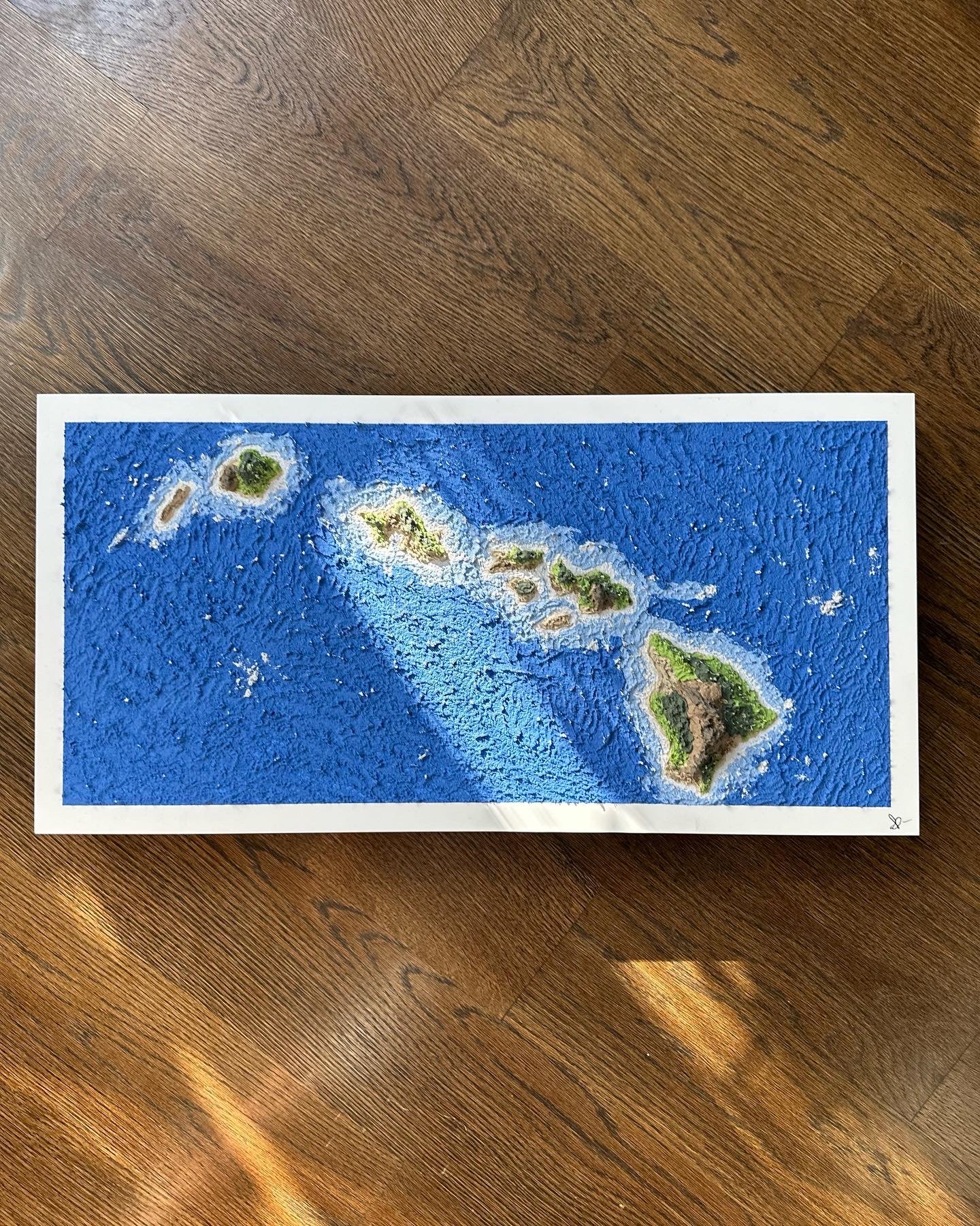 A printed map of the Hawaiian Islands with a blue background, showing the layout of the islands from north to south, placed on a wooden surface.