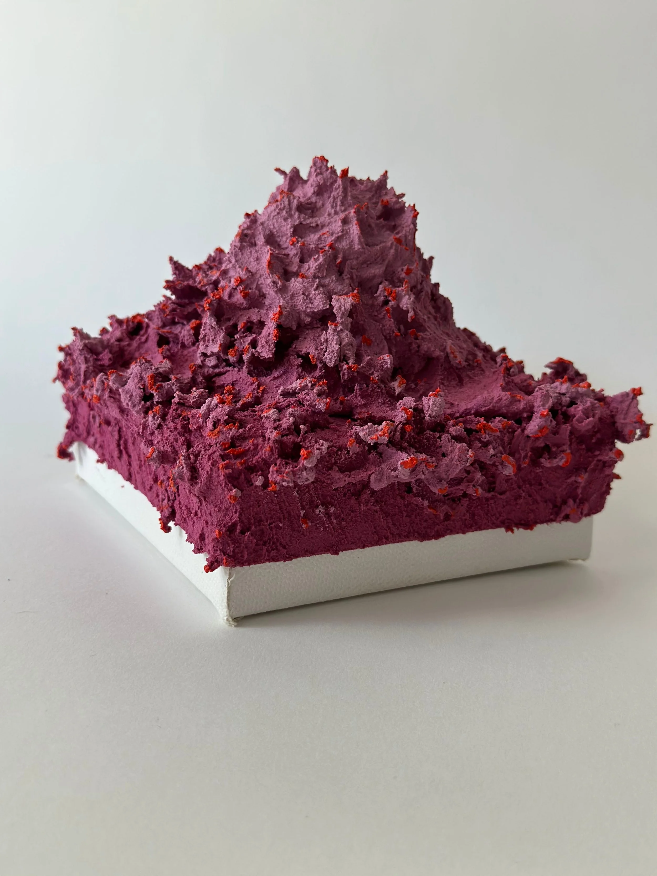 A slice of purple dessert with a textured, fluffy top and red sprinkles in a white paper tray.