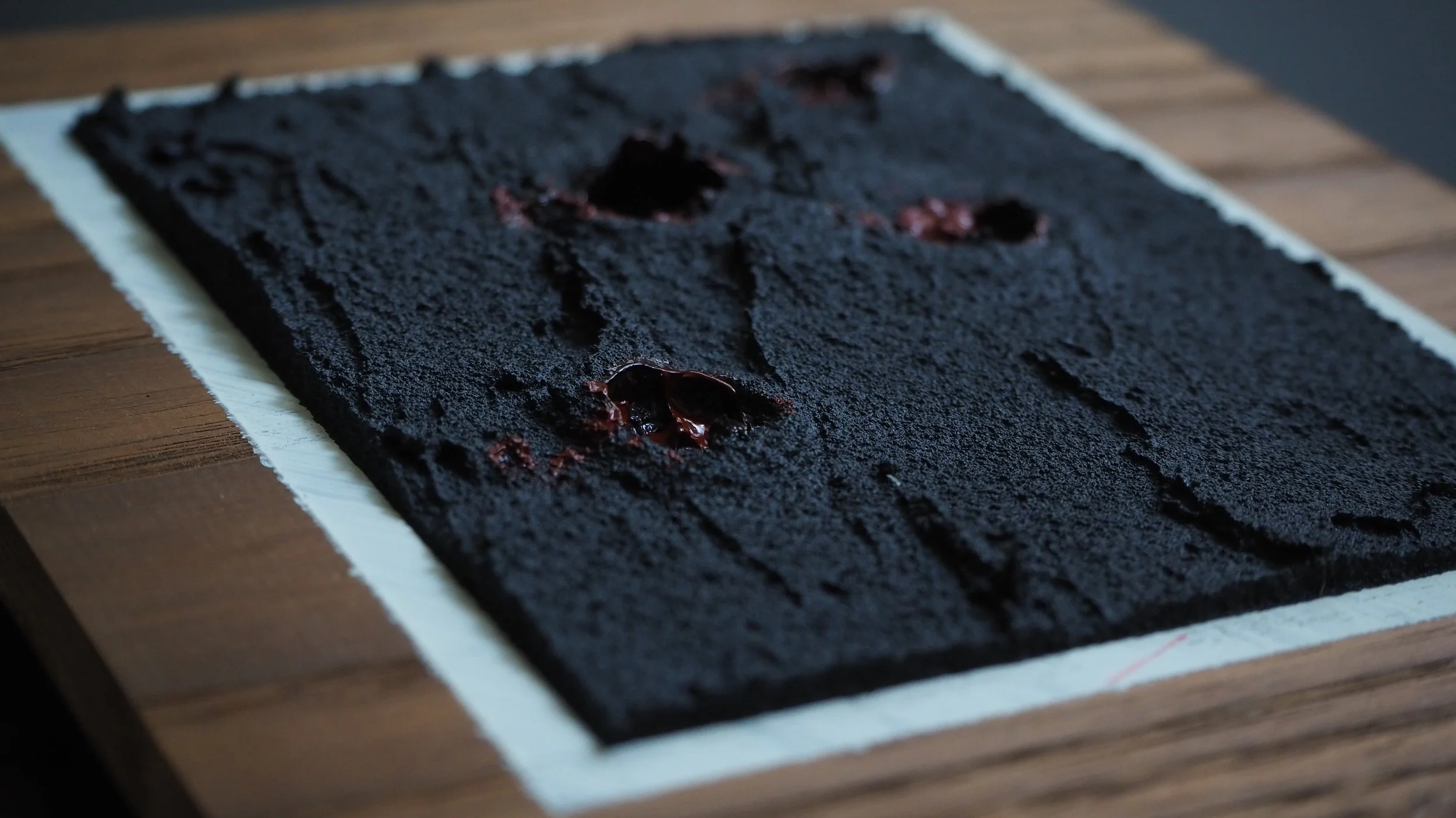 Close-up of a dark textured surface on a black slate-like material with red and black dried flower petals, resting on a wooden table.