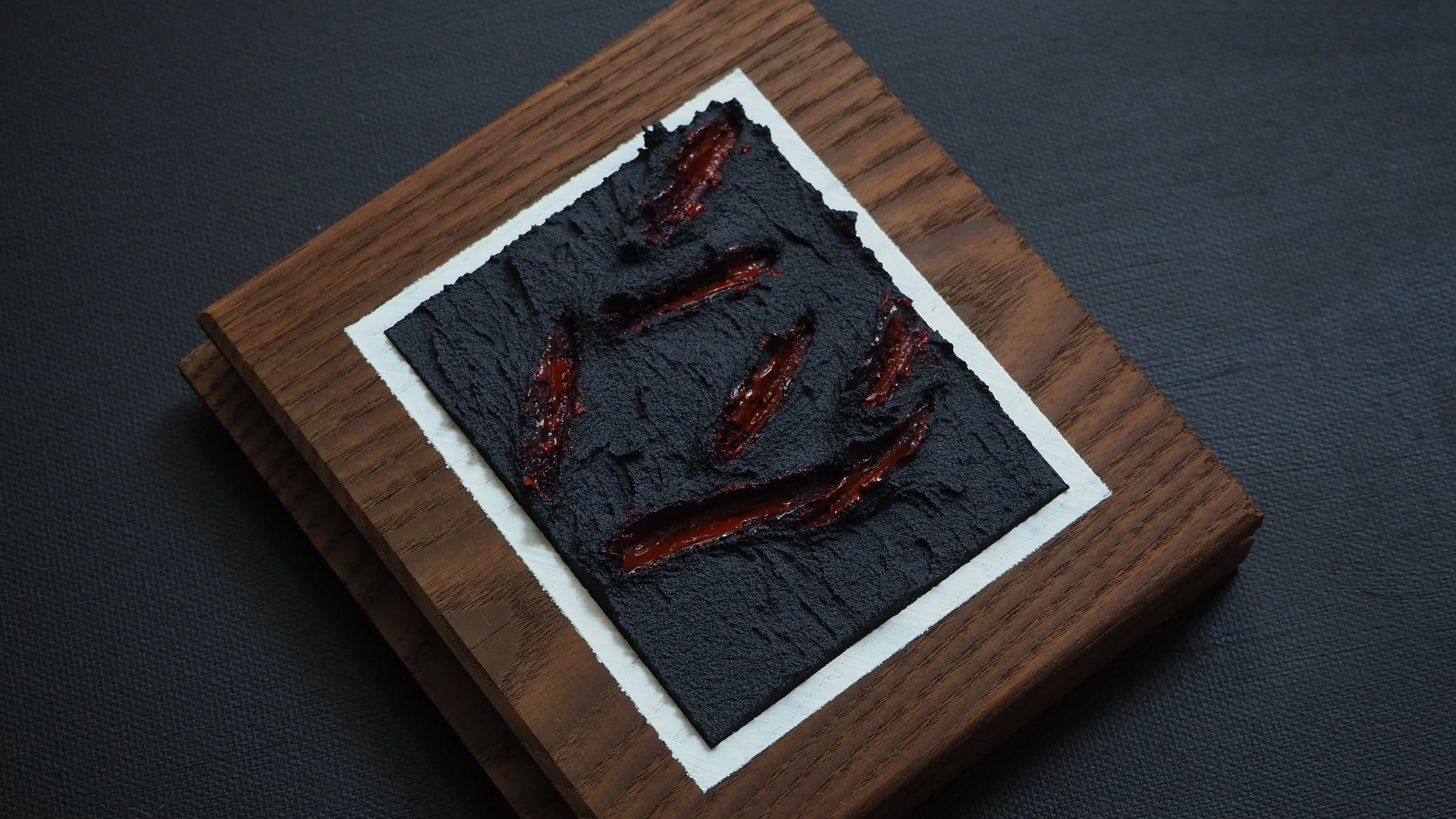 A piece of black toast with red jam on top, placed on a white paper on a wooden serving board.