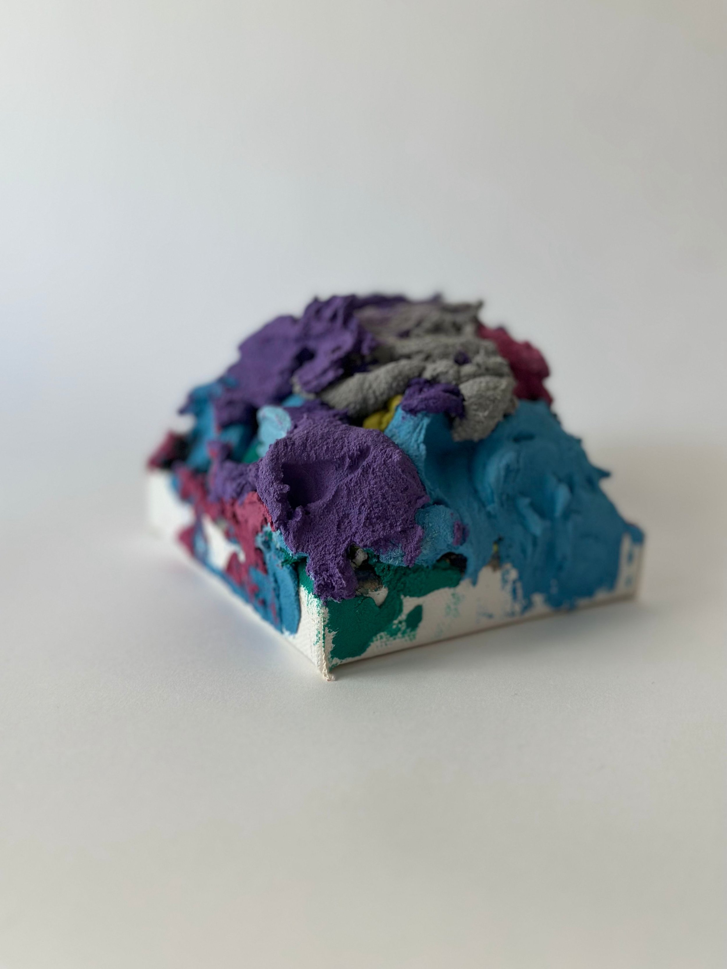 Colorful abstract sculpture with purple, blue, gray, pink, and yellow layers on a white base and background.