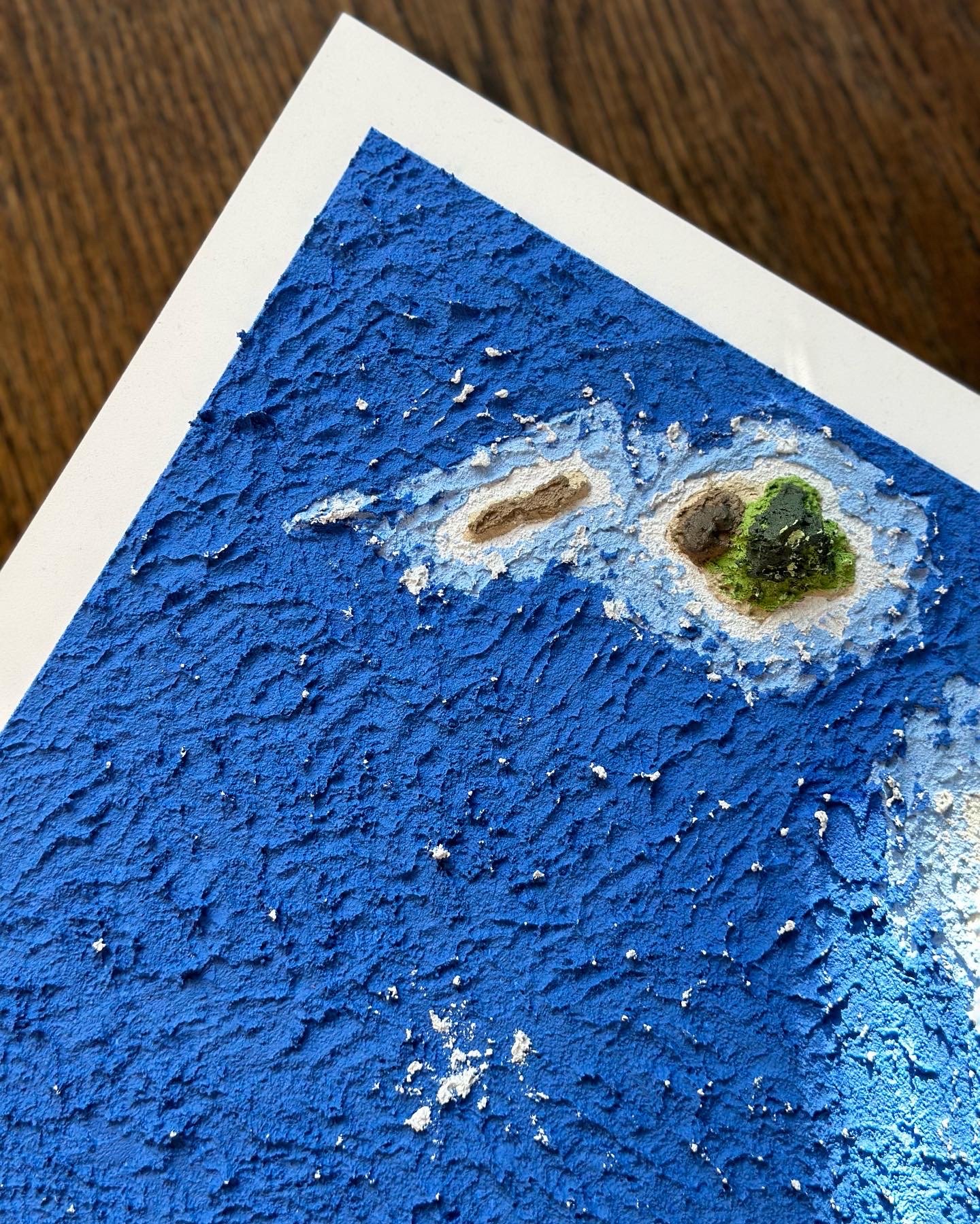 Close-up of a textured surface with a blue background and three small objects, resembling a miniature landscape or abstract art piece, on the surface.