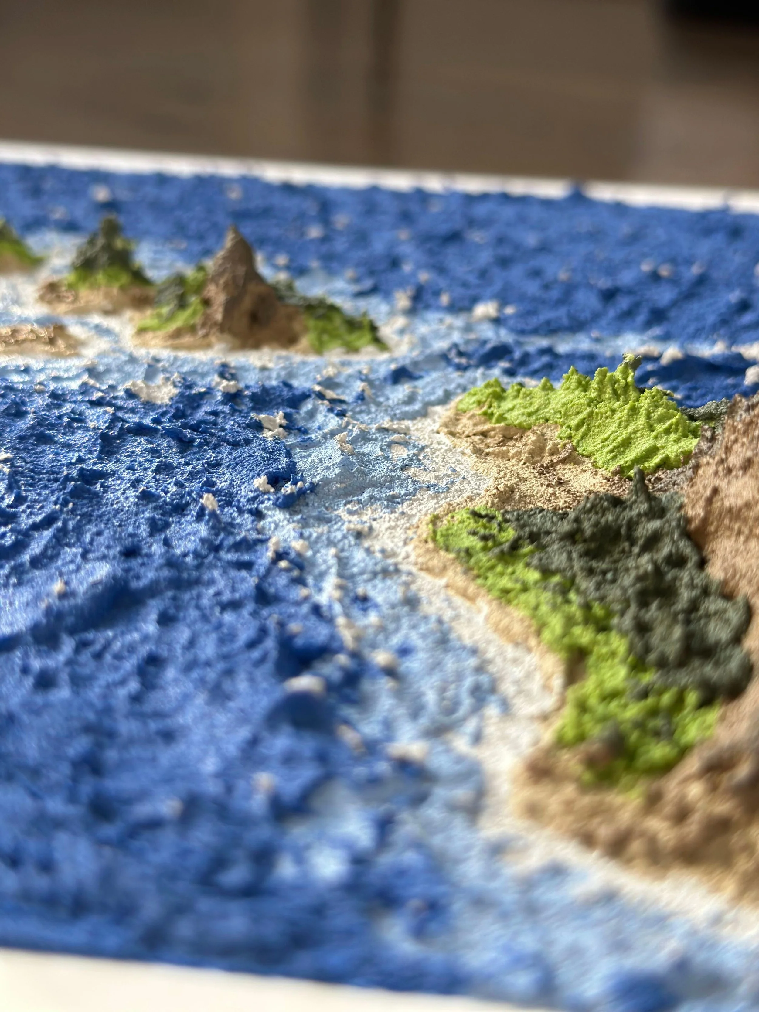 A detailed miniature topographical map with colorful textured terrain representing hills, mountains, and water bodies.