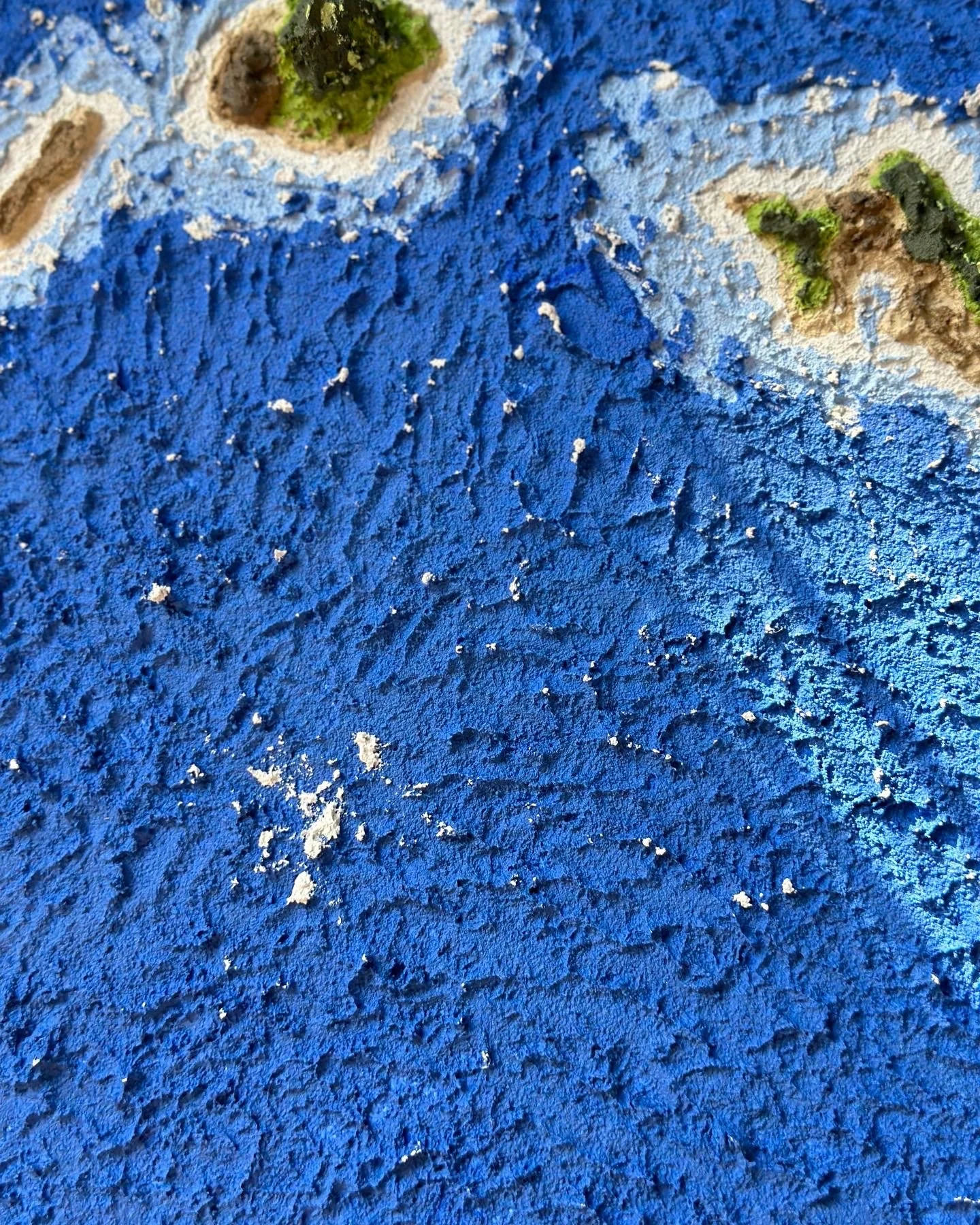 Close-up image of a blue painted textured surface with some patches of green paint and rough areas.