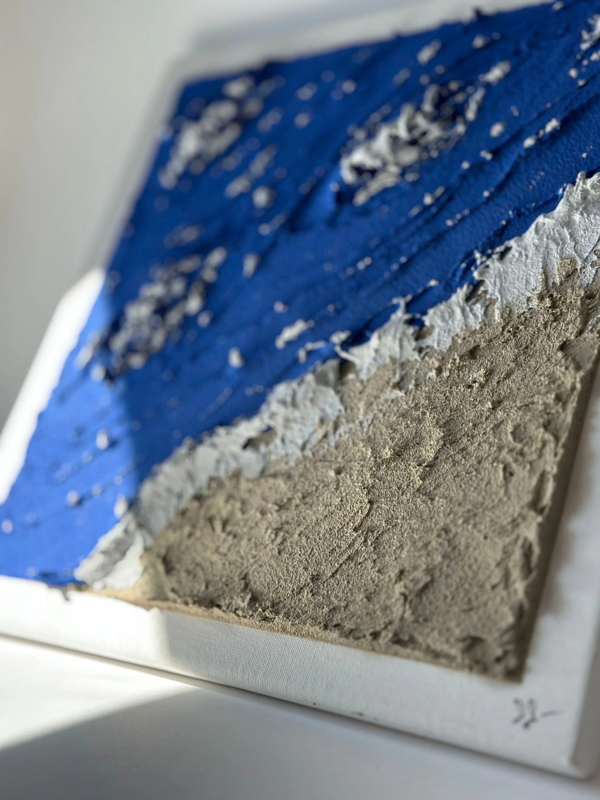 Close-up of textured layered painting on canvas with blue, white, and gray tones.