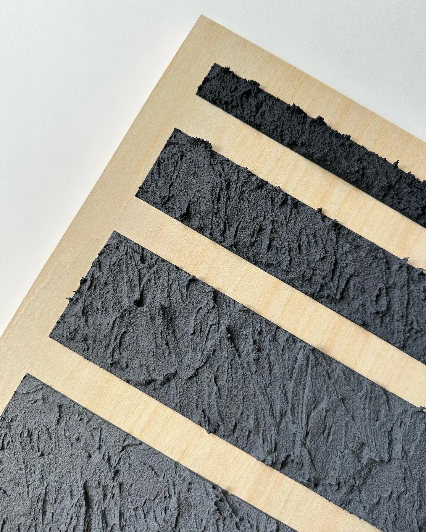 Samples of black textured paint or plaster swatched on wooden boards, arranged in a gradient from smallest to largest.
