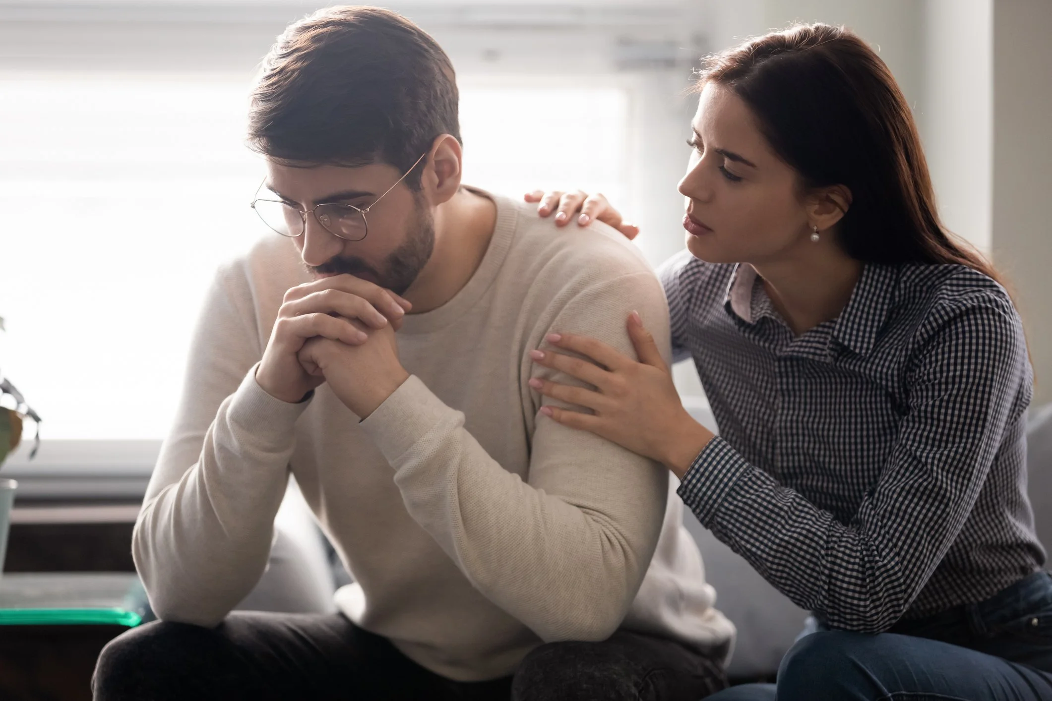 A woman is comforting a man who appears to be upset or sad, placing her hand on his shoulder and leaning in towards him.