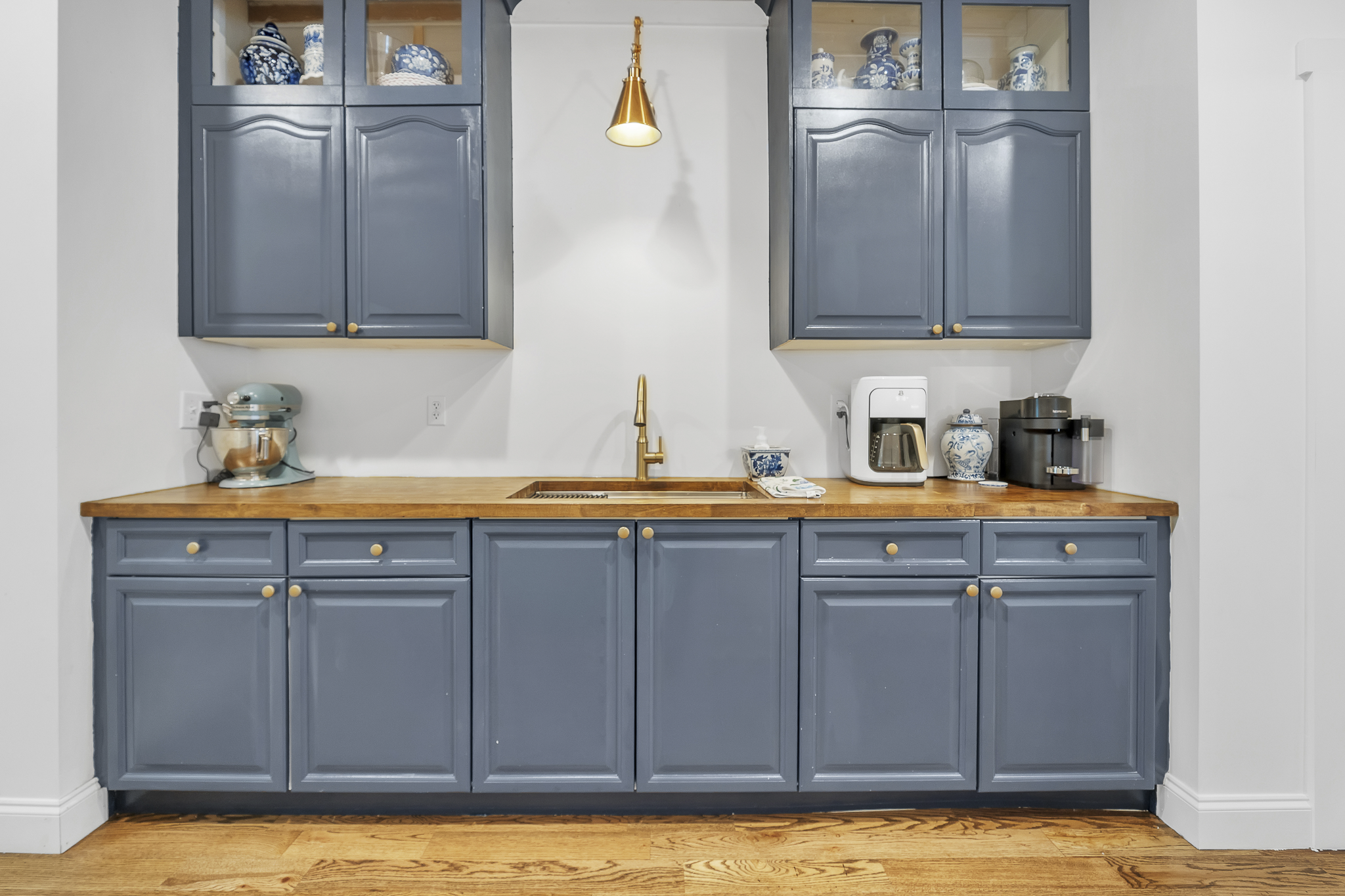 Blue kitchen cabinets with a wooden countertop, kitchen appliances, and decorative porcelain jars.